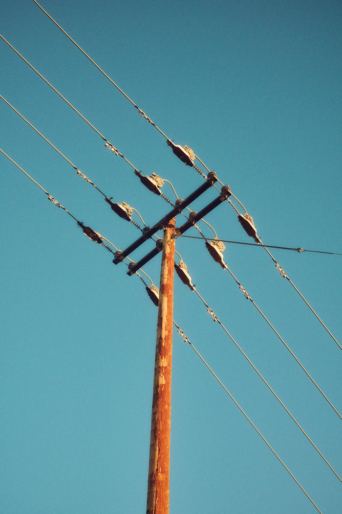 A wooden telephone pole with electrical wires set against a clear blue sky, captured in minimalistic style.